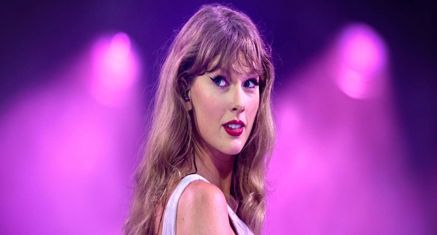 Taylor Swift performs onstage under purple lights.