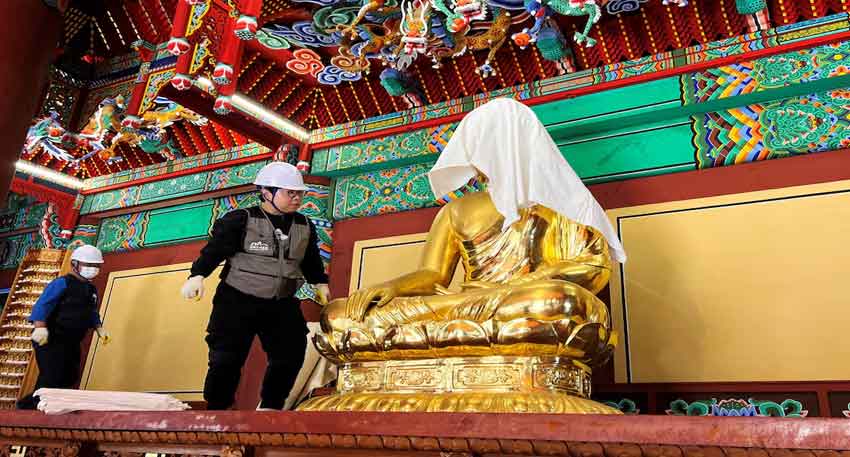 What led to the destruction of a historic South Korean temple? An official wraps Buddha statue with a fire-retardant blanket to protect it from a wildfire in South Korea