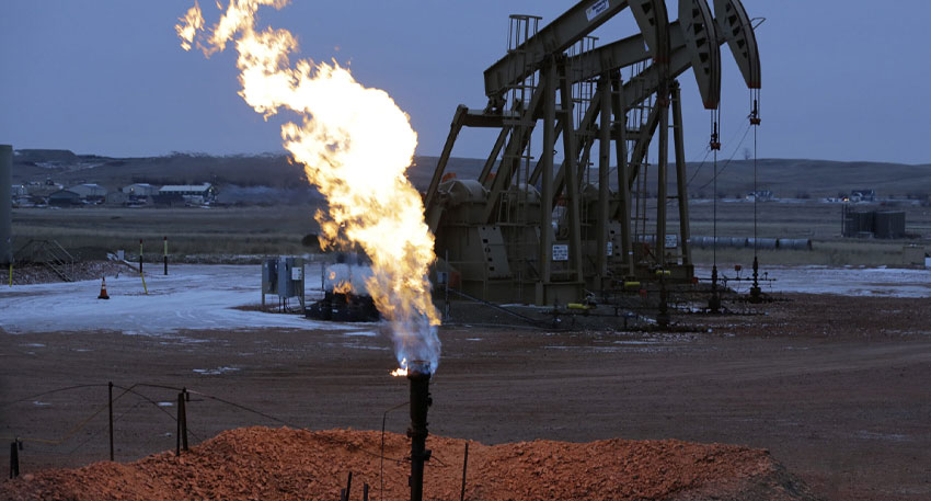 Gas flaring from a flare stack with oil pumpjacks behind it