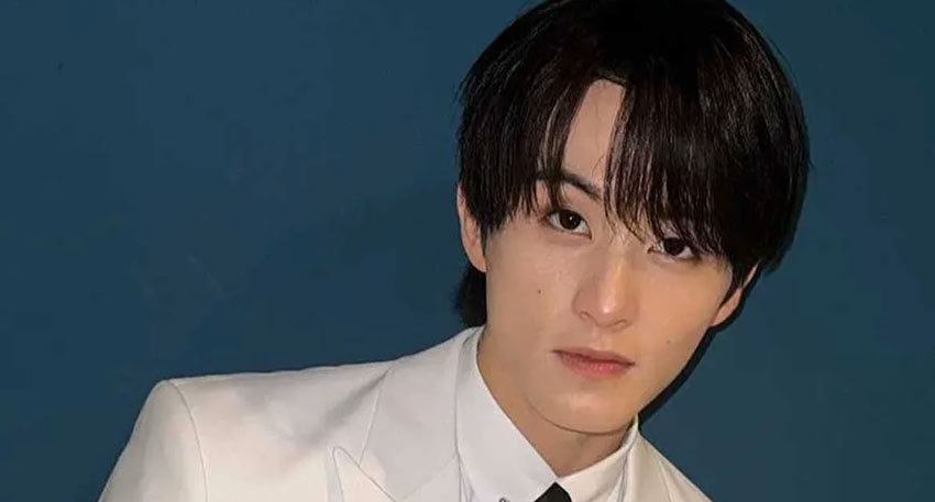 K-pop star Mark Lee posing in a white suit and black tie against a dark blue background.