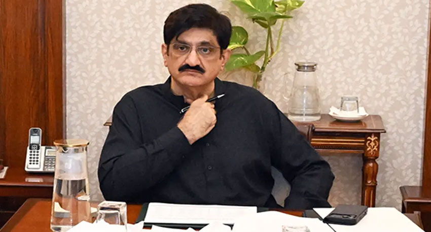 CM Sindh Murad Ali Shah in a black shirt, seated at a desk with documents and a pen, in an office setting.