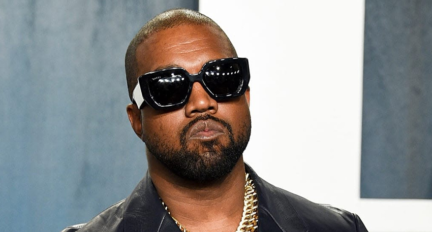 Kanye West wearing black sunglasses and a gold chain, looking forward.