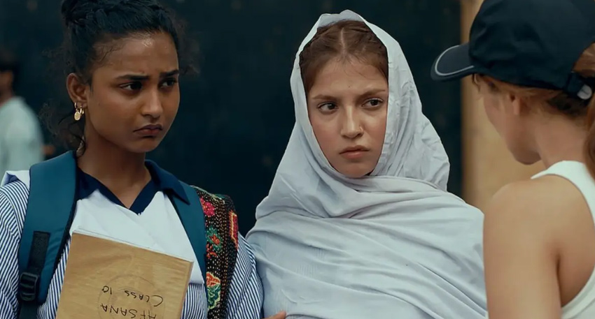 : Two girls in Lyari with serious expressions, one holding a book labeled 