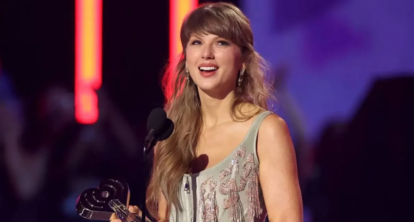 Taylor Swift smiling on stage at the 2026 iHeartRadio Music Awards in a mint green beaded corset.