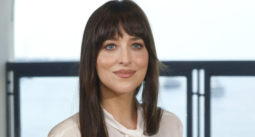 Dakota Johnson smiles in a white blouse with dark bangs and long hair, appearing in a viral video clip.