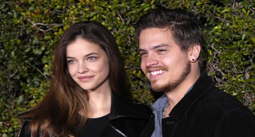 Barbara Palvin and Dylan Sprouse smiling together at a red carpet event in front of a green hedge background.