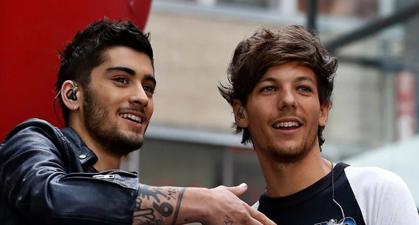 Zayn Malik and Louis Tomlinson of One Direction smiling together on stage during a performance.