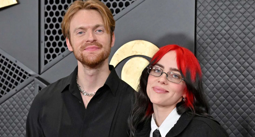 Billie Eilish with red and black hair standing next to her brother Finneas O'Connell at an event.