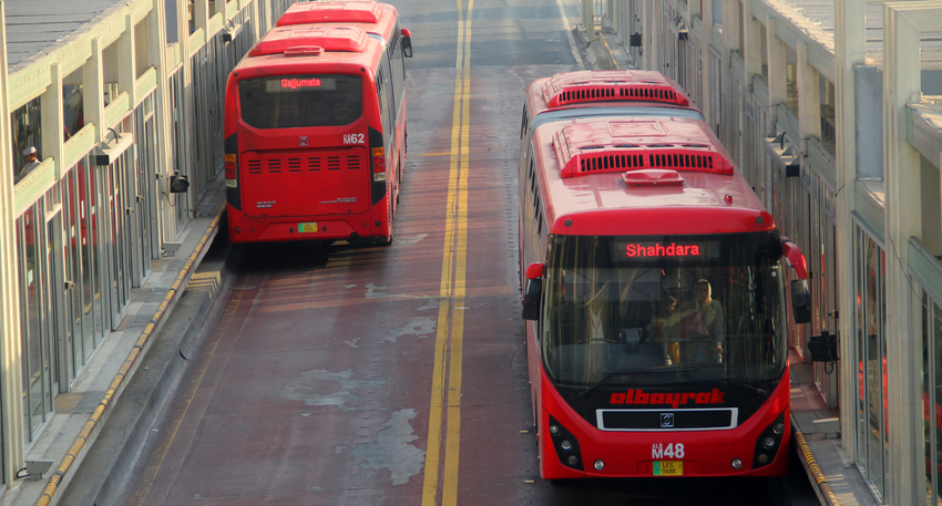 Red Lahore Metrobus bound for Shahdara at a station terminal.