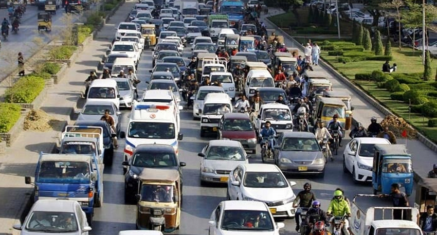 Heavy traffic congestion with cars, rickshaws, and motorcycles tightly packed on a multi-lane city road.
