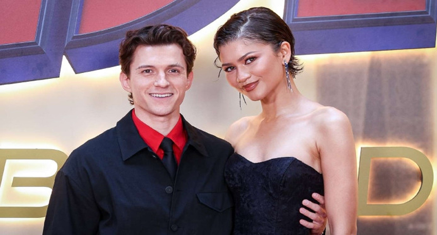 Tom Holland and Zendaya smiling together on a red carpet.