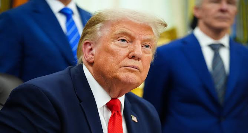 Donald Trump sitting in a navy suit and red tie.