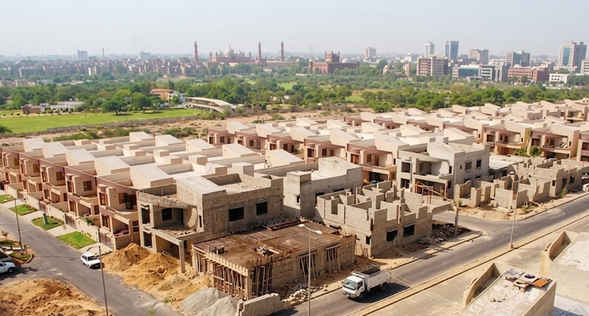 Rows of newly constructed grey brick houses under a clear sky in Pakistan.