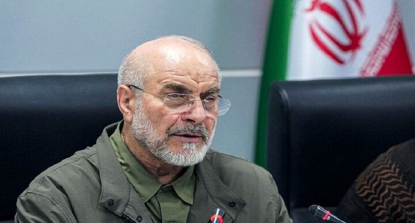 Mohammad Bagher Ghalibaf speaking at a conference with an Iranian flag in the background.