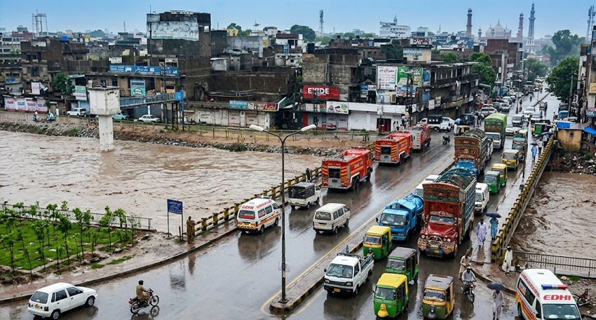 Vehicles and emergency services cross a bridge over a rising, muddy Nullah Lai river during heavy rains.