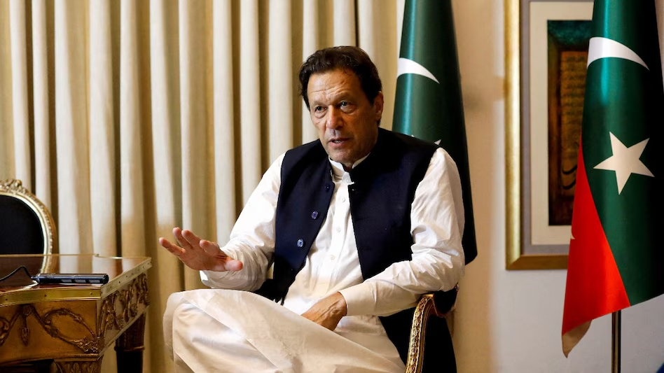 Imran Khan sitting in a chair wearing a white shalwar kameez and dark waistcoat.