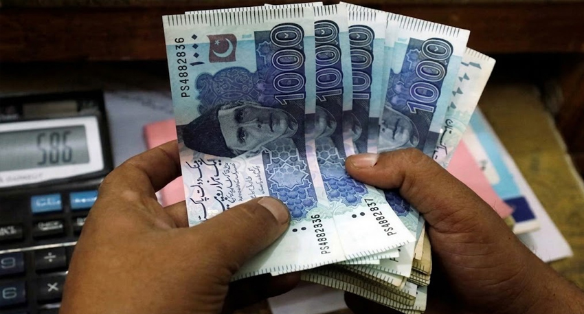 Hands holding a fan of 1000 Pakistani rupee bank notes next to a calculator.