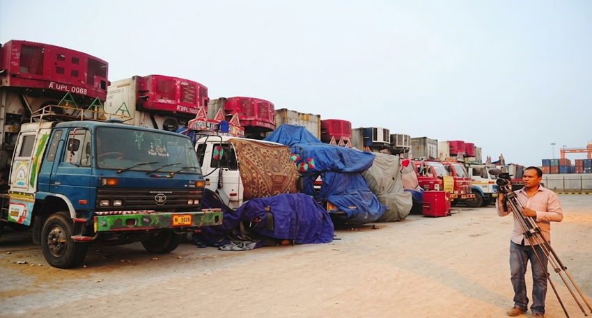 Line of parked cargo trucks at a port with a cameraman filming in Karachi.