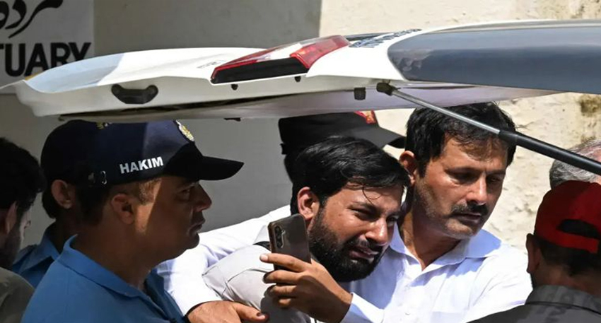 Grieving men gathered near a vehicle at the PIMS mortuary following a hospital tragedy.