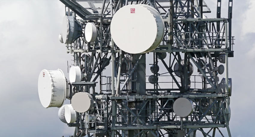 Close-up of a dense telecommunications tower structure equipped with multiple round white microwave and satellite dishes.