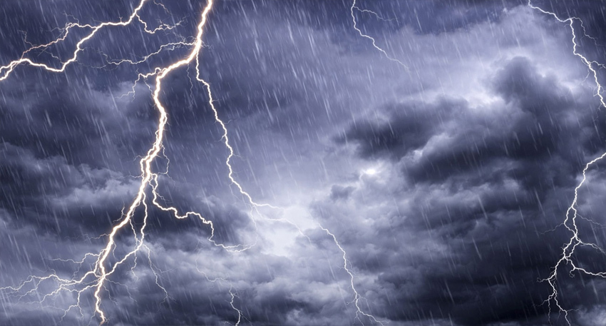 Heavy rain falling from dark storm clouds illuminated by multiple bright lightning bolts.