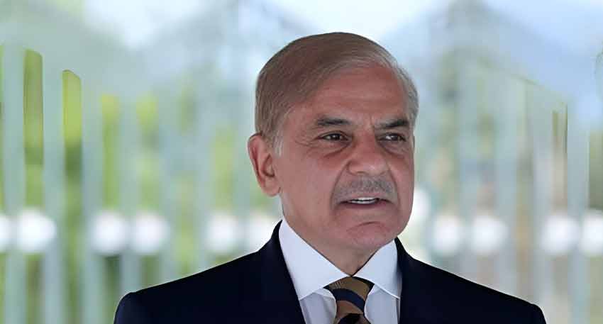 Close-up of Prime Minister Shehbaz Sharif wearing a navy suit, white shirt, and striped tie in a bright setting.