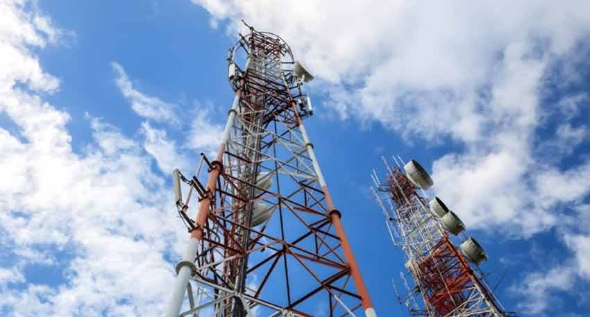 Two large red and white telecommunication towers with multiple antennas against a blue sky with white clouds.
