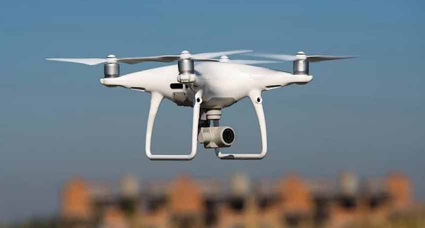 A white DJI Phantom 4 drone with a camera flying against a blue sky.