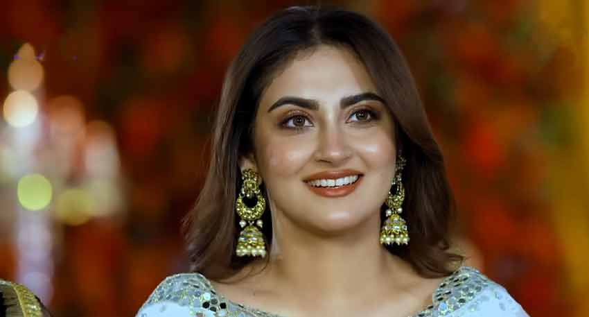 Pakistani actress Hiba Bukhari smiles in an embroidered blue outfit and traditional gold jhumka earrings.