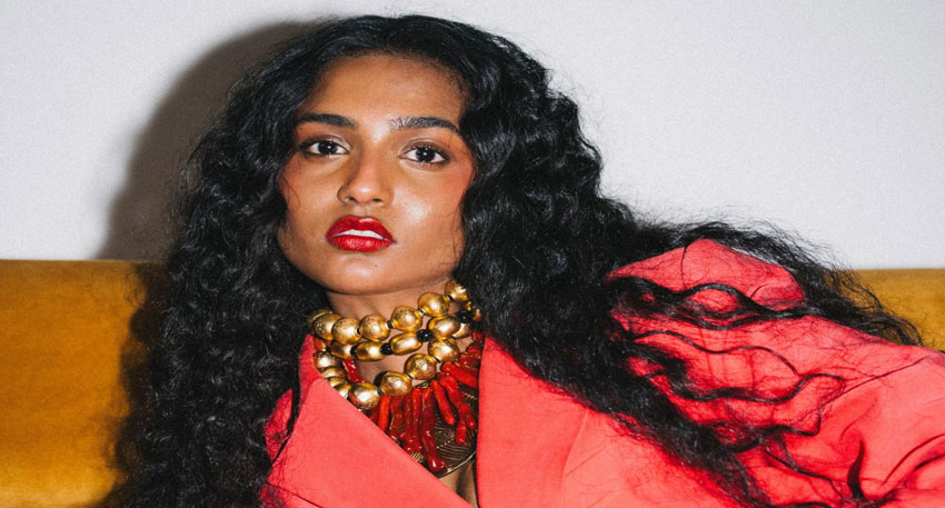 Pakistani model Trinette Lucas with curly black hair wearing a red blazer and statement necklace, photo: google