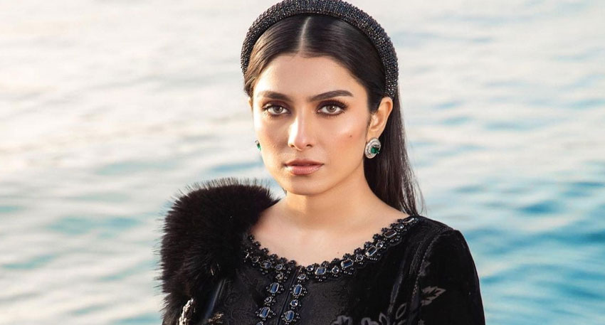 Ayeza Khan in a black velvet outfit with a beaded headband and green earrings, posing by the water. Photo, File photo