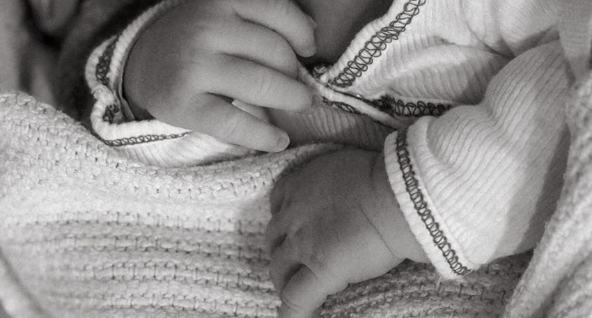 Close-up black and white photo of a baby's hands, wrapped in a textured blanket and wearing a shirt with dark stitching. Photo: Imam's Instagram