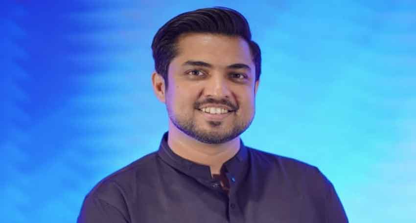 Pakistani journalist Iqrar Ul Hassan smiles while wearing a dark blue shirt against a blue background.