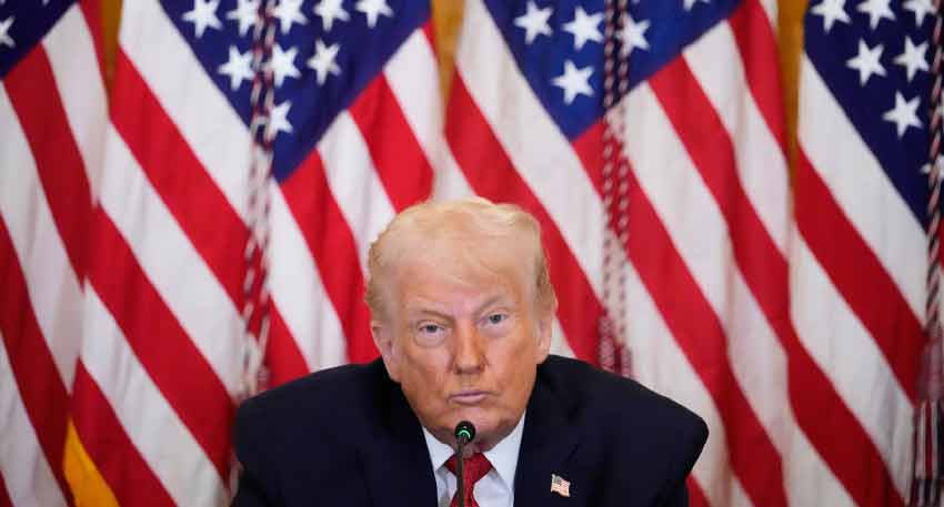Donald Trump seated in front of a row of American flags during a press conference or speech.