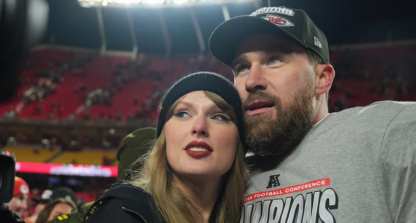 Taylor Swift and Travis Kelce leaning together at a football stadium.