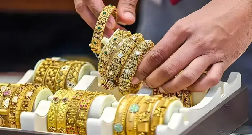 Ornate gold bangles displayed on a white tray as a jeweler's hands lift a stack of jewelry.
