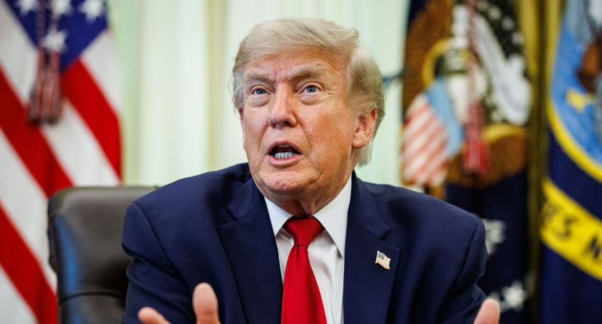 Donald Trump speaking behind a desk with flags in the background.