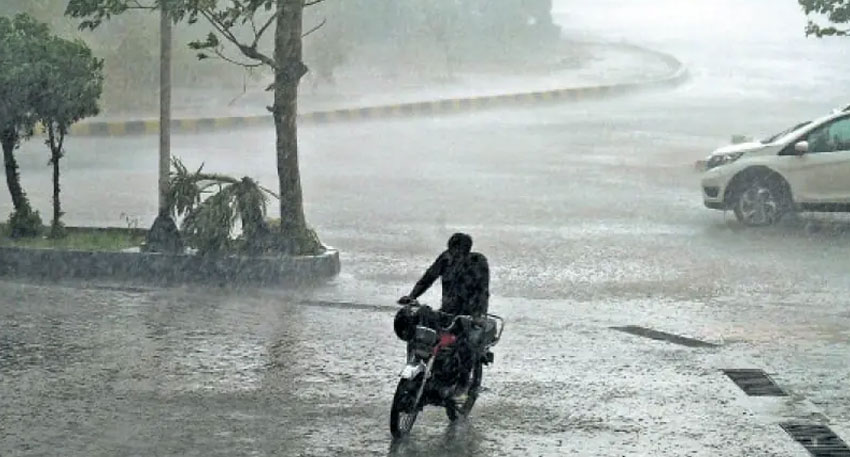 Motorcyclist navigating heavy rain on a flooded Lahore street.
