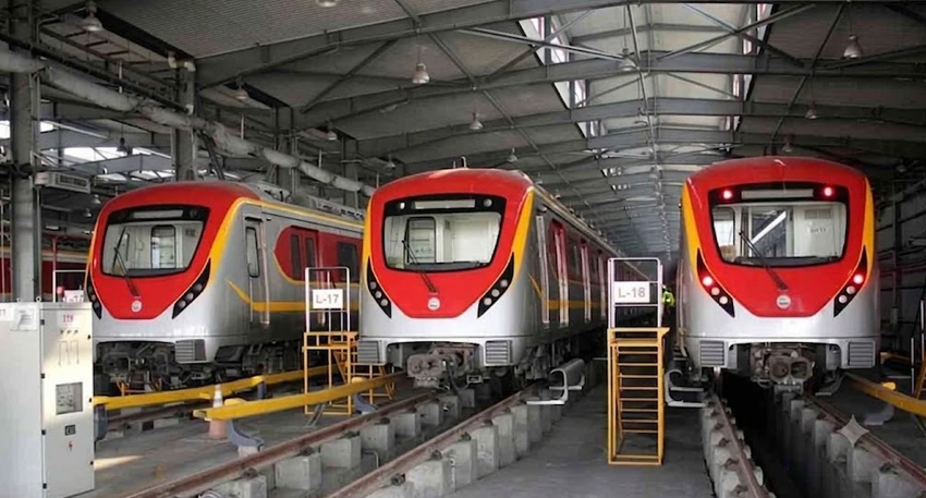Three red and silver Lahore Orange Line metro trains parked inside a maintenance depot.