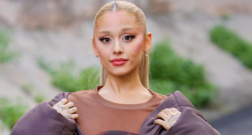 Ariana Grande posing outdoors wearing a brown top and matching jacket.