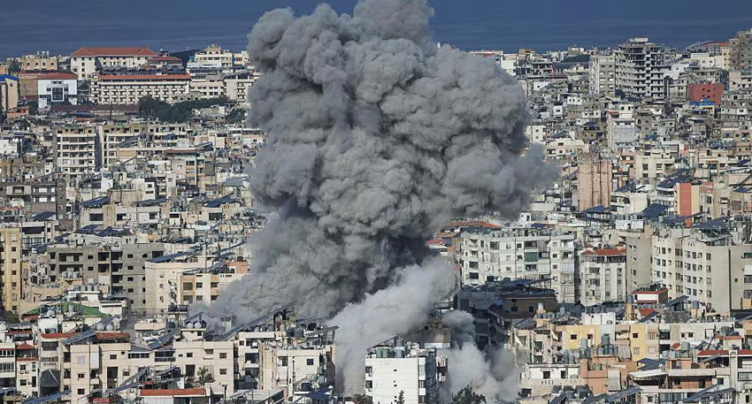 Huge plume of grey smoke rising over a dense coastal cityscape following an explosion.