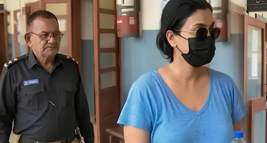 Anmol Pinky, wearing a blue shirt and black mask, walking past a Punjab Police officer in uniform.
