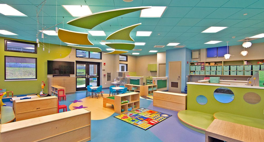Modern colorful daycare interior with wooden shelves, bright mats, and green hanging ceiling acoustic clouds.