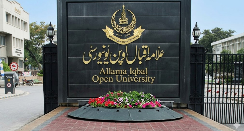 Allama Iqbal Open University sign with gold lettering and a floral display in front.