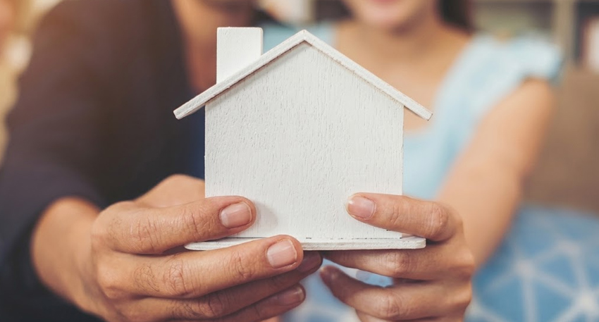 Couple holding a small white wooden house model.