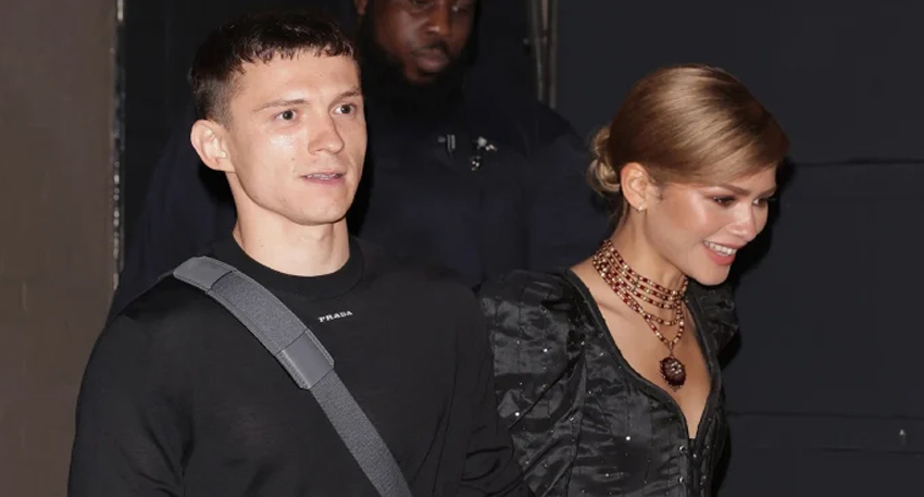 Tom Holland and Zendaya walking together in stylish black outfits at an evening event.