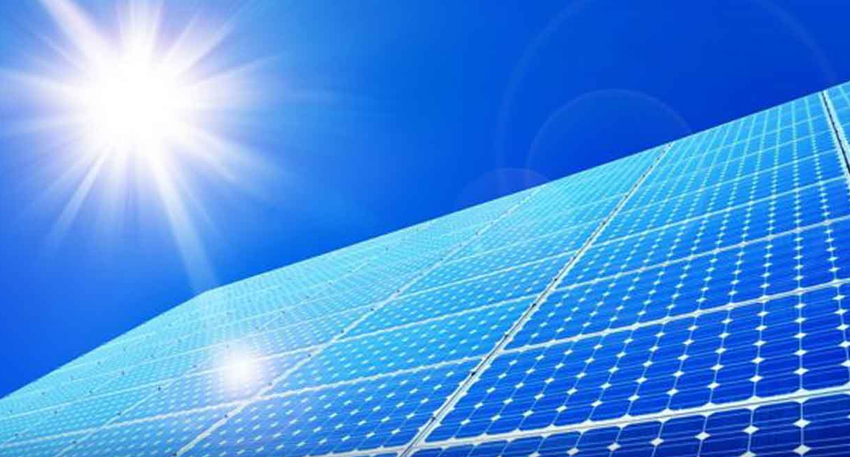 Large array of blue solar panels angled toward a bright sun in a clear sky.