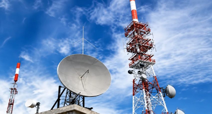 Large satellite dish and red-and-white telecommunications towers against a blue sky with wispy clouds.