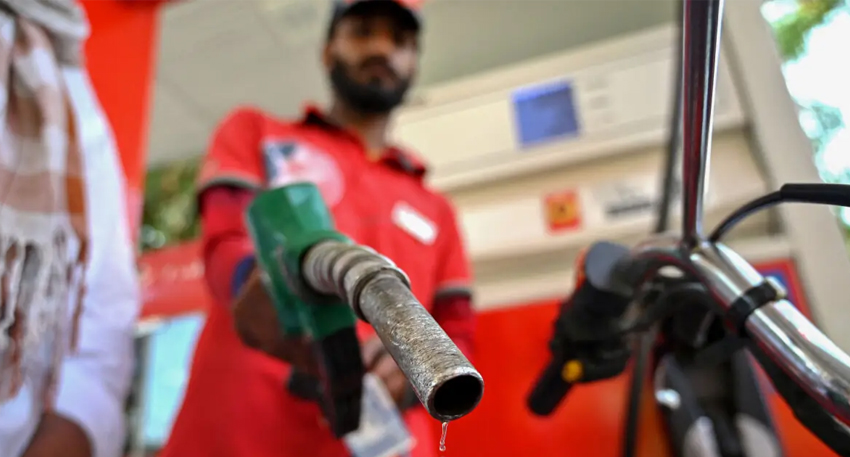 Gas station worker holding a green fuel nozzle with a droplet of gasoline hanging from the tip.