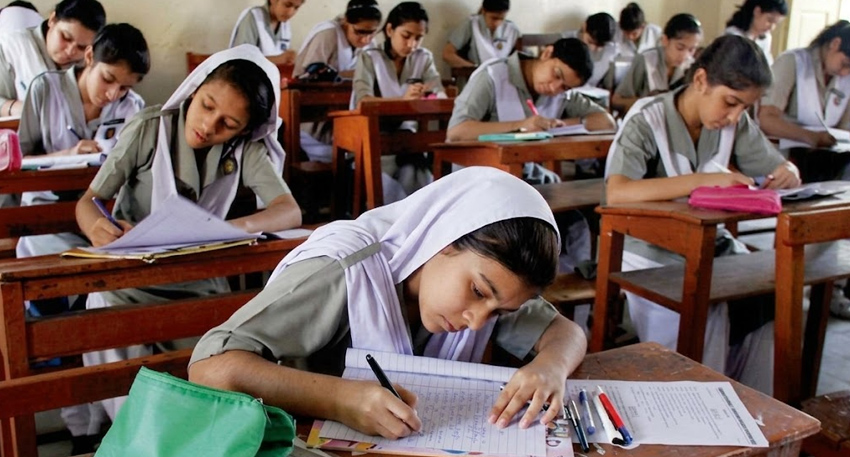 Female students in uniforms and hijabs taking an exam in a classroom.